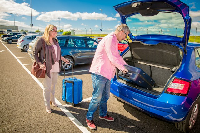Muškarac i žena stavljaju kofere u otvoreni prtljažnik plavog automobila na parkingu